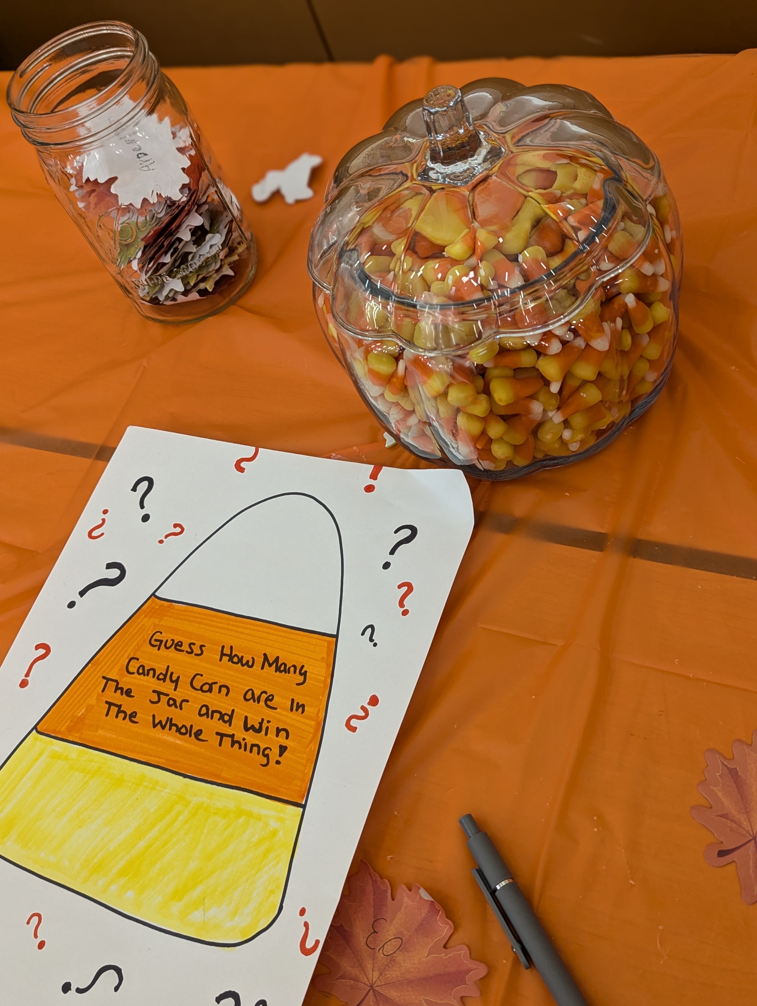 A jar of candy corn sits next to a sign that reads "Guess how many candy corn are in the jar and win the whole thing!"
