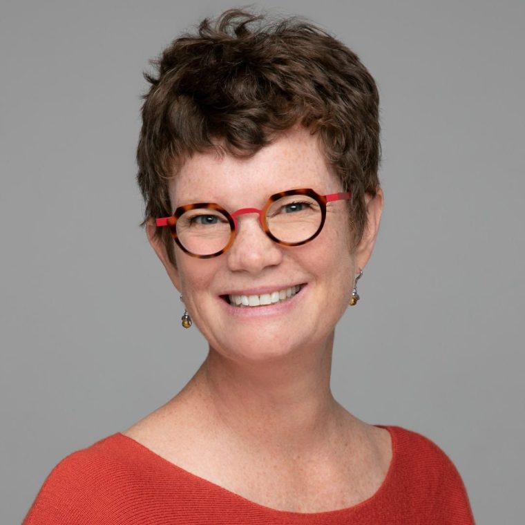 Headshot of Amy Lang, a white woman with short brown hair, wearing a red shirt and matching red eyeglasses.
