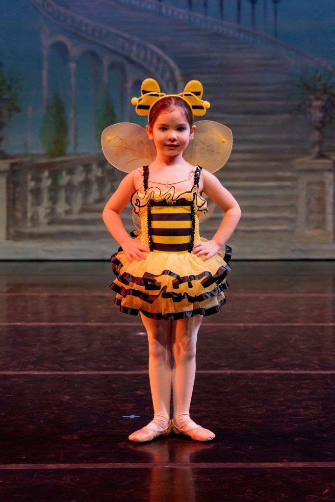 Lillian poses on stage as a honeybee in a yellow dress with black stripes and wings.