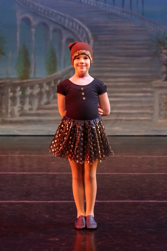 Demi poses on stage wearing a black shirt and skirt with gold sparkly polka dots and a cap.